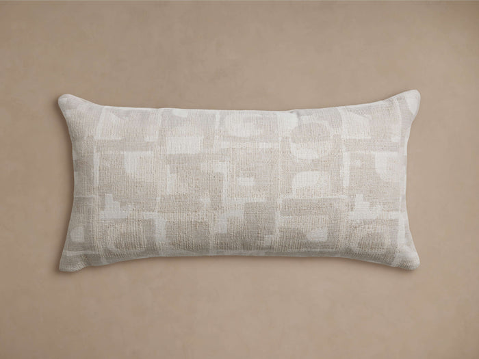 Marli Outdoor Lumbar Pillow. Rectangular, beige & off-white monochromatic woven pillow with abstract geometric pattern, on tan background.