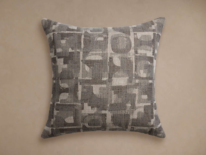 Marli Outdoor Pillow: Square, monochromatic gray/silver abstract pattern with woven texture, laid flat against a neutral wall.