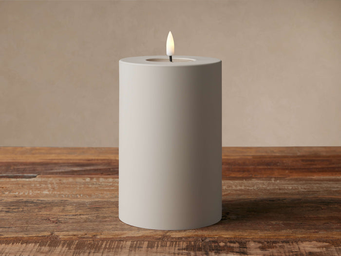 Matte Taupe LED candle, cylindrical, with a realistic flickering flame & faux melted wax pool, on a rustic wood surface.