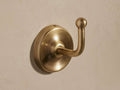 Maxwell Hook, antiqued brass, mounted on a light wall. Rounded base, curved arm with a spherical tip, facing right.