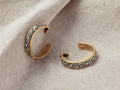 Maylin Hoop Earrings featuring gold-plated brass with textured pyrite accents, displayed on a soft fabric background.