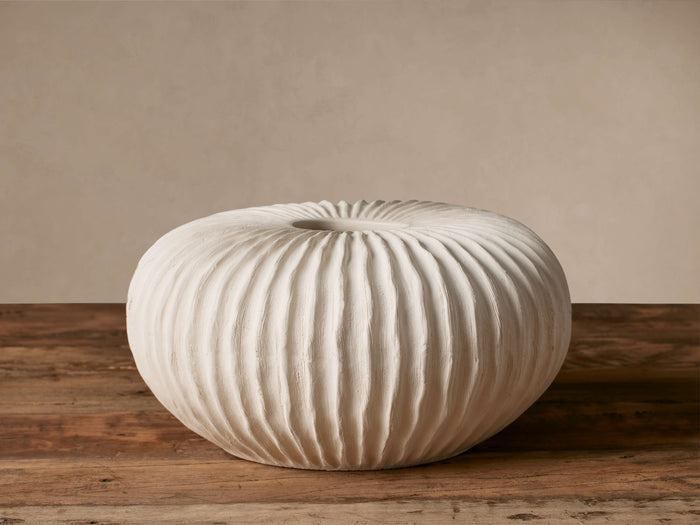 Meadow Vase, round, off-white ceramic with deeply ribbed texture, on a rustic wooden surface against a light wall.