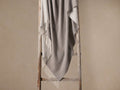Melange Cashmere Throw draped on a rustic wooden ladder. The two-sided grey blanket features elegant white fringe details.