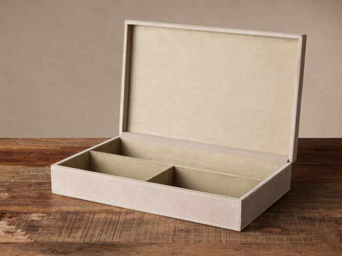 Open light greige Meline Suede Box with white stitching, revealing three tan suede interior sections, on a wooden surface.