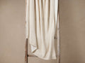 Merin Ribbed Knit Throw in cream, draped over a rustic wooden ladder, showing its soft, vertical ribbed knit texture.
