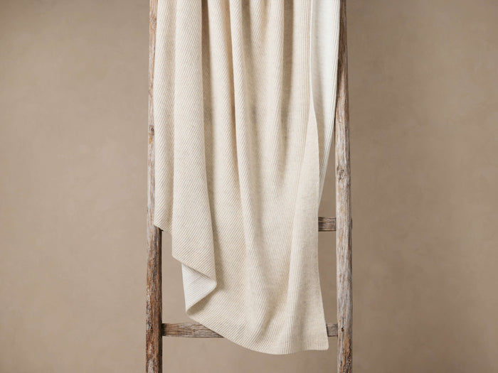 Merin Ribbed Knit Throw in cream, draped over a rustic wooden ladder, showing its soft, vertical ribbed knit texture.
