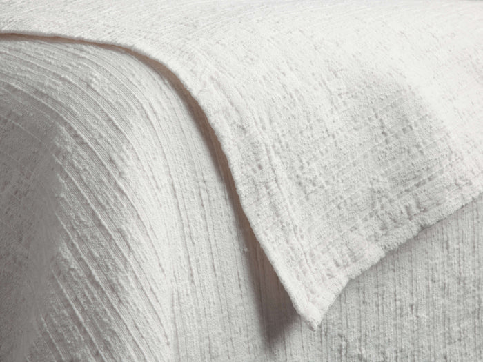 Close-up of a white Mihali Matelasse Quilt, showing its distinct textured, woven pattern with subtle raised lines and bumps.
