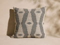Montara Outdoor Pillow: Square woven pillow with a gray-blue & beige ikat pattern, upright on a neutral background.