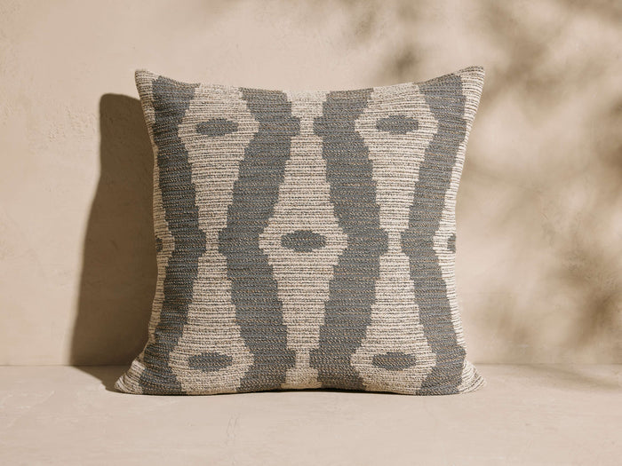 Montara Outdoor Pillow: Square woven pillow with a gray-blue & beige ikat pattern, upright on a neutral background.