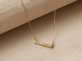 Morgana Gold Pendant Necklace with a horizontal rectangular gold bar set with small raw diamonds on a delicate chain, placed on fabric.