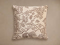 Moura Pillow: Square, light beige woven pillow with a brown abstract wavy pattern, centered on a neutral taupe background.