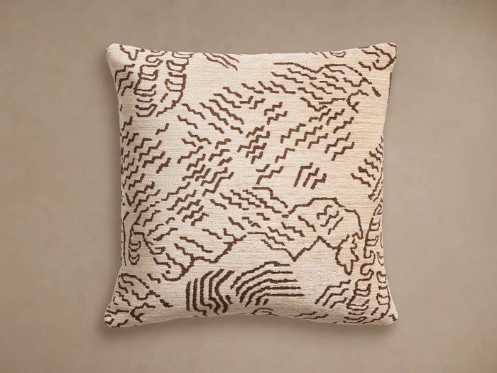Moura Pillow: Square, light beige woven pillow with a brown abstract wavy pattern, centered on a neutral taupe background.