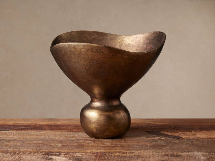 Myles Footed Bowl, antiqued brass finish, organic sculptural shape with flowing edges and a round foot, on a rustic wood surface.