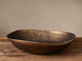 Myles Round Bowl made of cast aluminum with a textured antiqued brass finish, sitting on a rustic wooden table against a neutral wall.