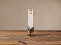 Myles Taper Holder with an antiqued brass sculptural base, clear glass cloche, and a lit white taper candle on a wooden table.