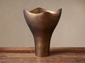 Myles Vessel: Textured antiqued brass cast aluminum decorative vessel with wavy, organic top, standing upright on wood.