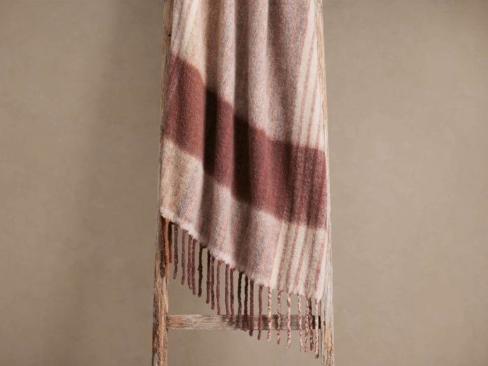 Soft, fringed throw blanket draped over a rustic wooden ladder. Features warm brown stripes on a light beige background, with long tassels.