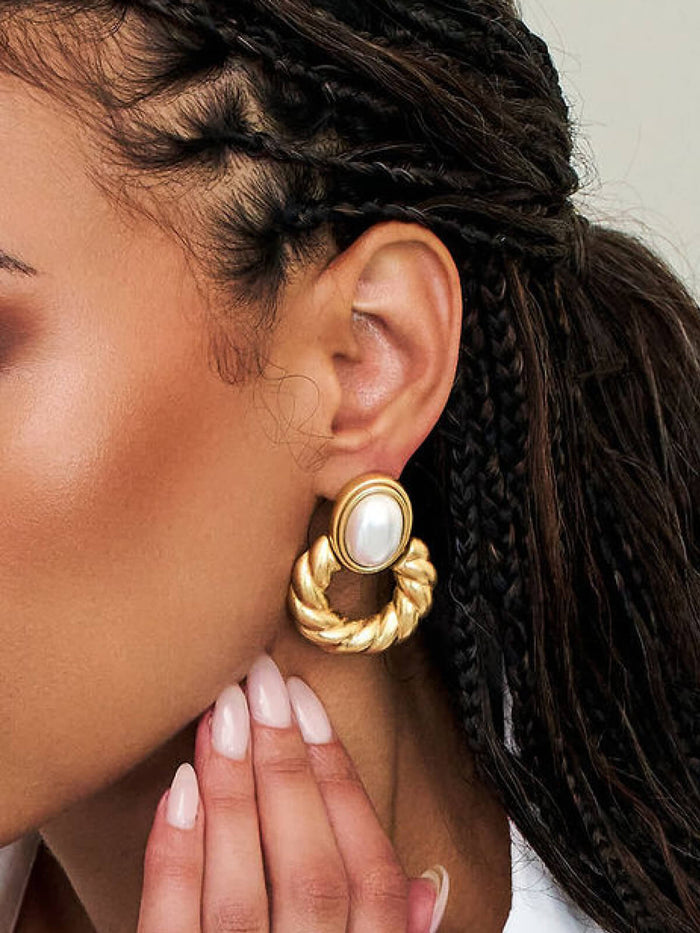 A close-up of a model wearing a large gold hoop earring with a central white pearl, showcasing the jewelry on the ear.