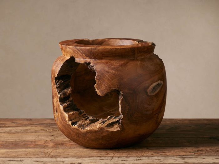 Natural Root Teak Vase: a rustic brown teak wood vase with a large, raw organic cavity on its front, sitting on a distressed wood table.