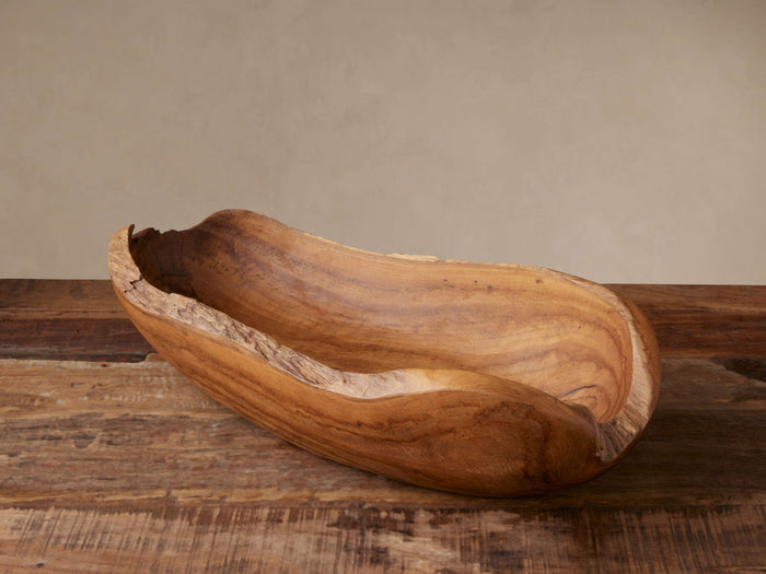 Natural Vanora Bowl, an elongated, rustic teak wood bowl with natural rough edges, shown on a wooden surface.
