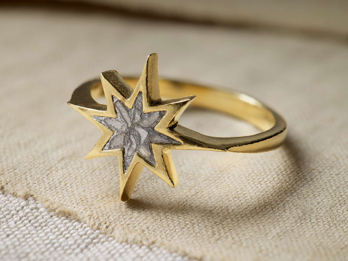 Close-up of the gold Noelia Ring, featuring a star design with a textured gray center, resting on light beige fabric.