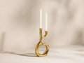 Gold-toned Nouria Open Base Double Taper Holder, organically shaped with an open center, holding two lit white candles.