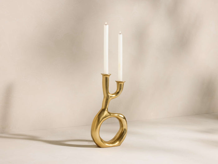 Gold-toned Nouria Open Base Double Taper Holder, organically shaped with an open center, holding two lit white candles.