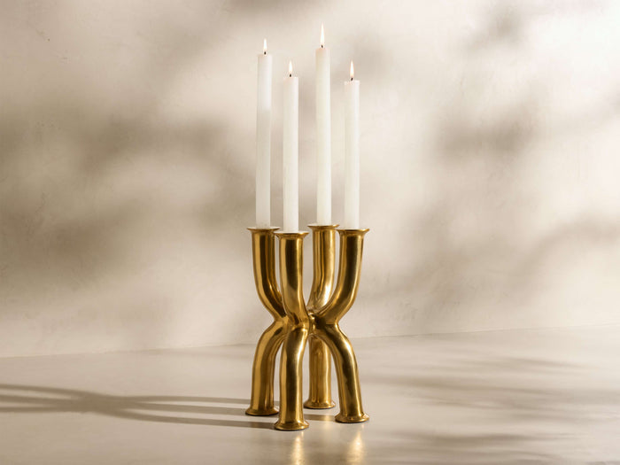 Front view of the golden brass finish Nouria Tall Quad Taper Holder with four lit white taper candles.