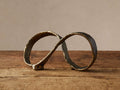 Nowles Sculpture, an antique brass distressed aluminum infinity symbol, sits on a rustic wooden table against a light wall.