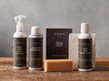 Arhaus Nubuck Leather Care Kit: spray Eco Protector, Degreaser can, Cleaner bottle, cloth box, white cloth, and sponge on wood.