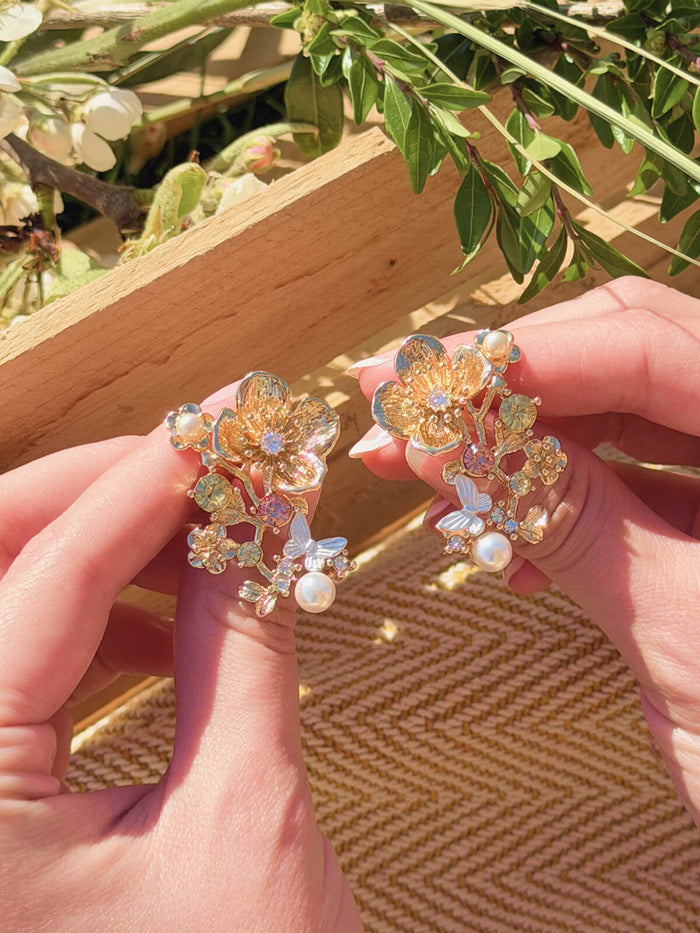Floral earrings held between fingers with a natural background