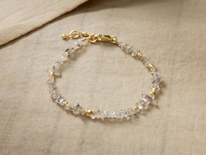 Oaklynn Bracelet with clear, raw Herkimer diamonds & small gold vermeil beads, delicate gold clasp, on light brown fabric.