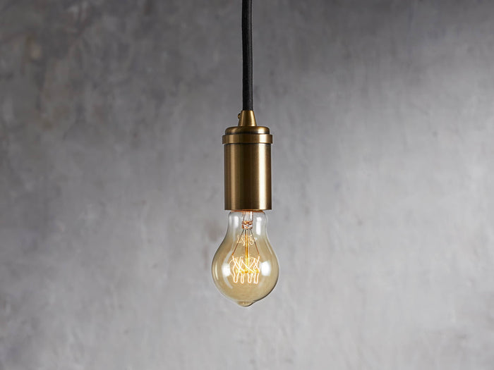 Ohlson Brass Swag Pendant with a brass-plated finish, hanging against a textured gray background.
