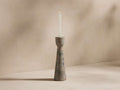 A tall, slender marble candle holder with a smooth, swirling pattern, holding a single lit white taper candle against a neutral background.