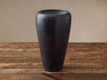Tall, dark gray Omo Marble Vase with a subtly tapered shape, natural veining, sitting on a rustic wooden surface against a neutral wall.