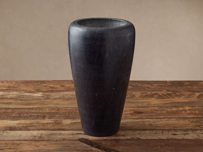 Tall, dark gray Omo Marble Vase with a subtly tapered shape, natural veining, sitting on a rustic wooden surface against a neutral wall.