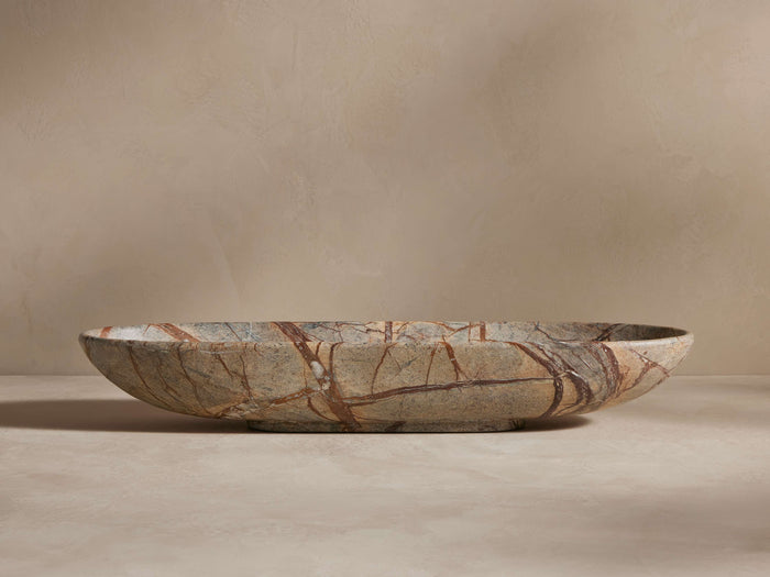A shallow, oval-shaped stone bowl with marbled brown and beige patterns on a beige background, showcasing its natural texture.