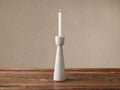 Omo Marble Taper Holder, light grey with subtle veining, holding a lit white candle on a rustic wood table.