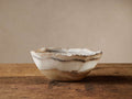 Onyx Bowl with a wavy, organic rim, showing natural cream, brown, and gray bands, sitting on a rustic wooden table.