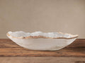 Oval Onyx Canoe bowl, translucent white with natural veining, raw, textured light brown edges on a rustic wooden table.