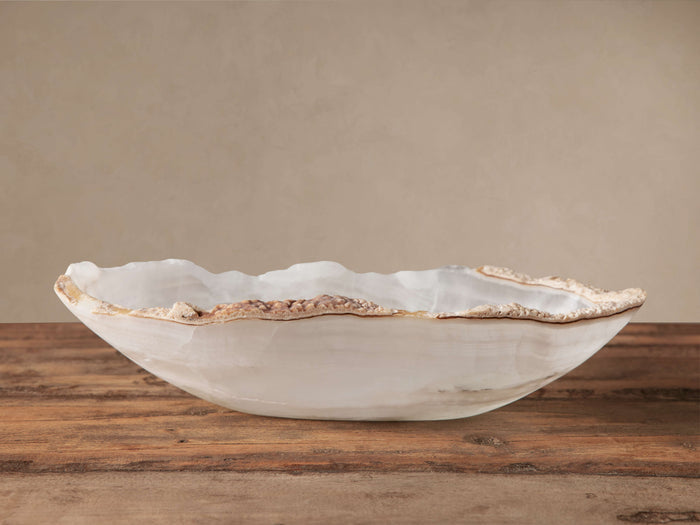 Oval Onyx Canoe bowl, translucent white with natural veining, raw, textured light brown edges on a rustic wooden table.