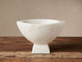 White marble Oslo Footed Bowl, hand-carved, with a flared top and solid rectangular foot, displaying natural veining on a wooden surface.