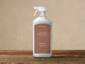 White Arhaus Outdoor Upholstery Protector spray bottle with a brown label, standing upright on a rustic wooden surface.
