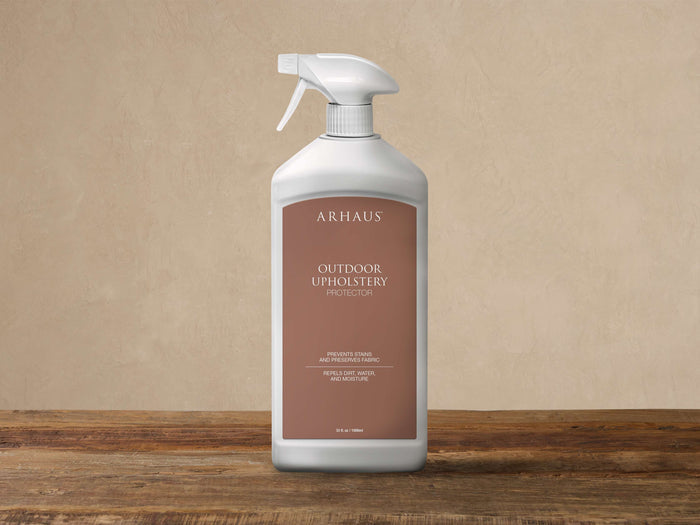 White Arhaus Outdoor Upholstery Protector spray bottle with a brown label, standing upright on a rustic wooden surface.