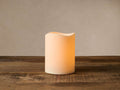 Single cream outdoor LED candle, glowing softly with a wavy top edge, standing on a textured wooden table.