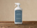 White ARHAUS Outdoor Marble & Stone Protector spray bottle with dark teal label, on a wooden surface against a light wall.