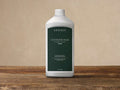 White plastic bottle of Arhaus Outdoor Teak Invisible Shield, 33.8 oz, with a dark green label, standing on wood.