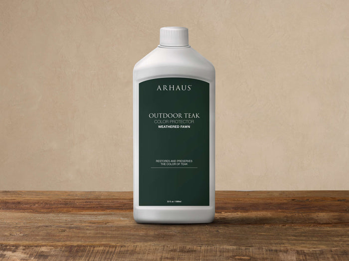 White bottle of Outdoor Teak Color Protector in Weathered Fawn, green label, upright on a rustic wooden surface.