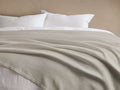Paden Linen Ribbed Bed Blanket in Dune, a light beige, ribbed textured blanket, elegantly draped over a bed with white pillows.