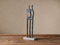 Abstract Pair Sculpture: matte black aluminum figures, one with circular cutout, standing on a rectangular white marble base.
